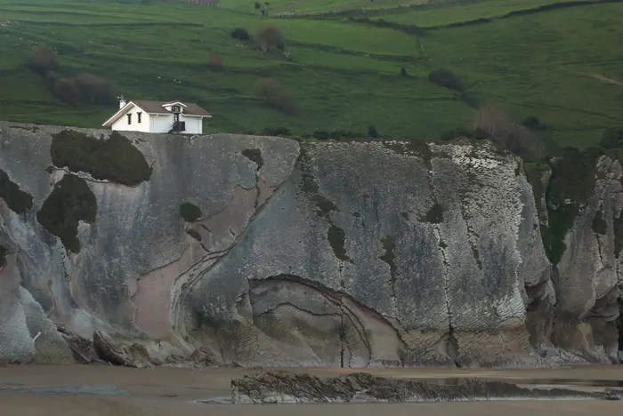 Une falaise de roche grise avec une maison blanche la surplombant.